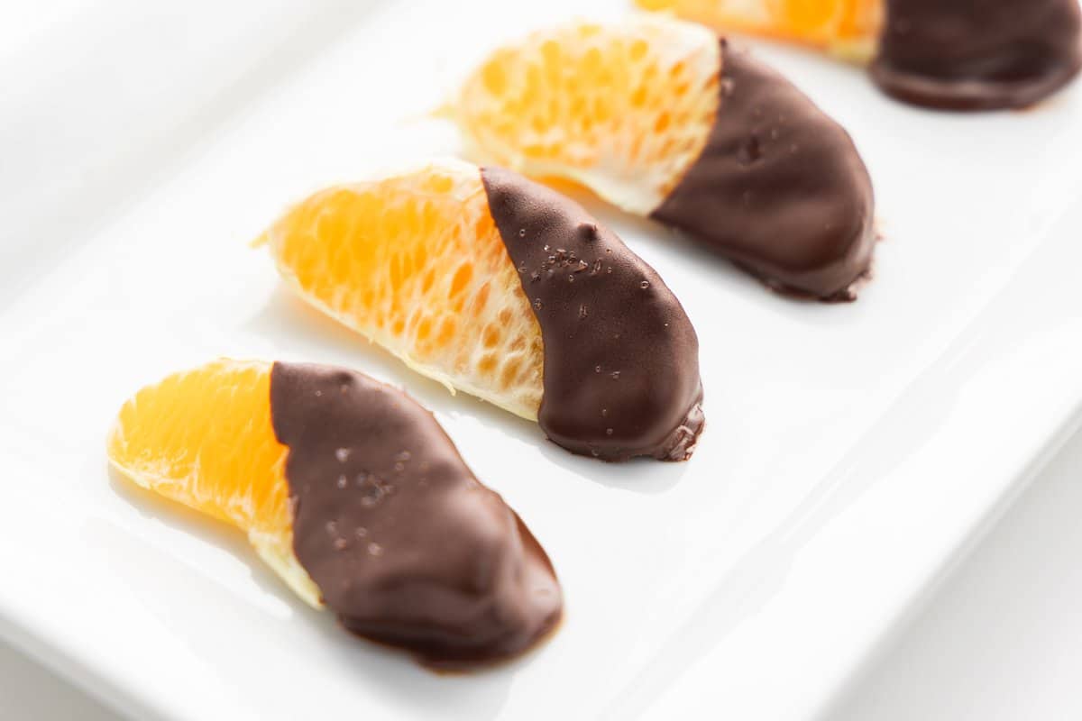 4 chocolate dipped clementines with sea salt on a plate.