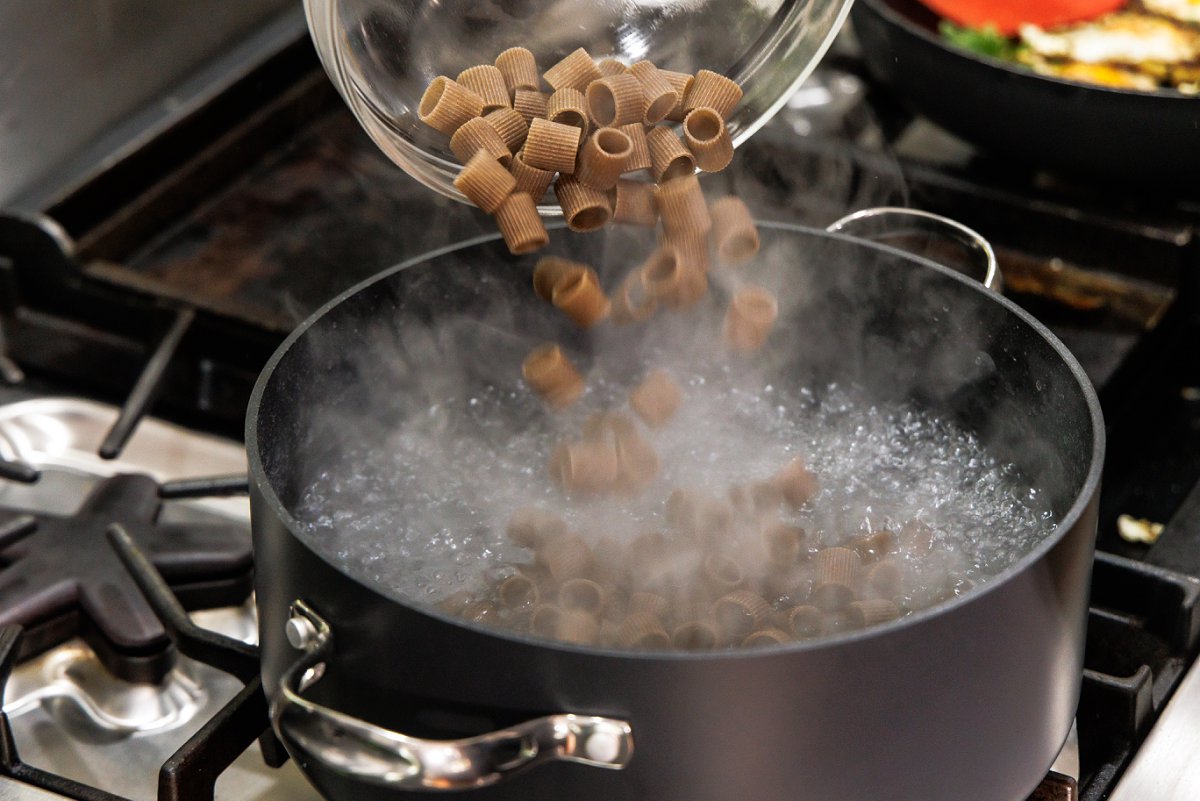 Adding whole wheat pasta to a pot of boiling water.