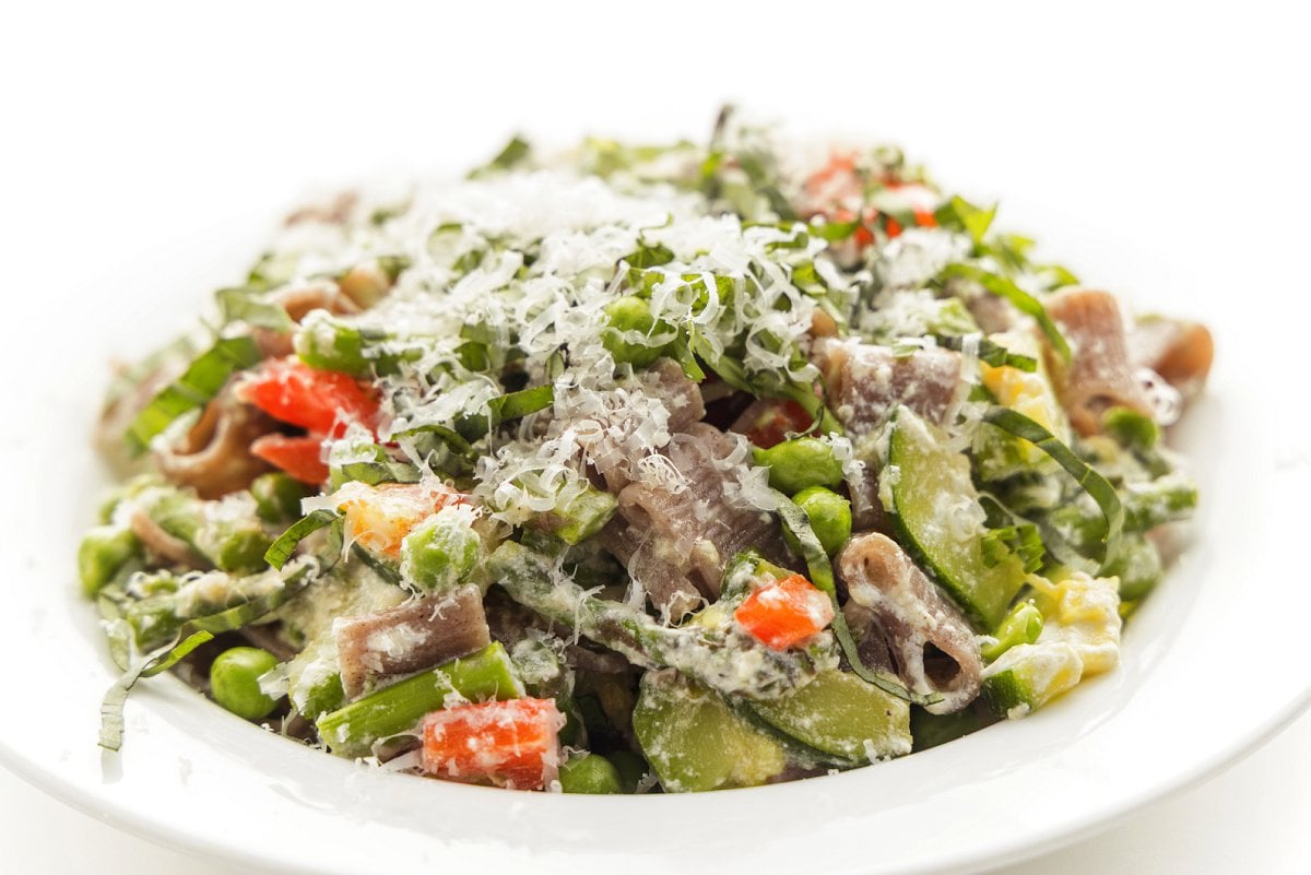 Primavera pasta with sautéed vegetables topped with freshly grated parmesan cheese on a plate.