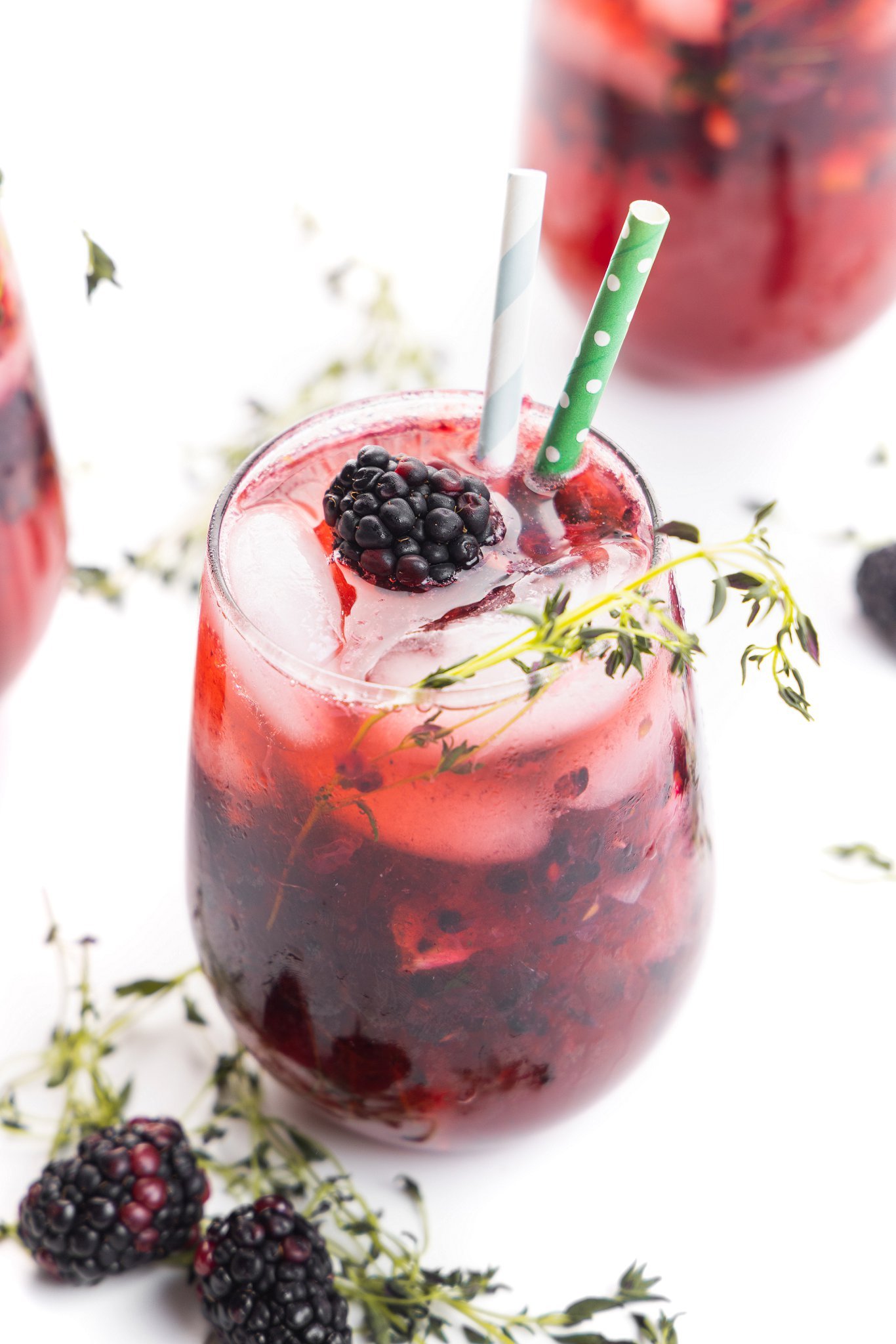 Blackberry ginger smash with thyme in a stemless wine glass with two paper straws.