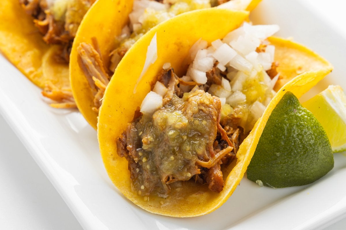 Tacos al pastor assembled on a plate with lime wedges.