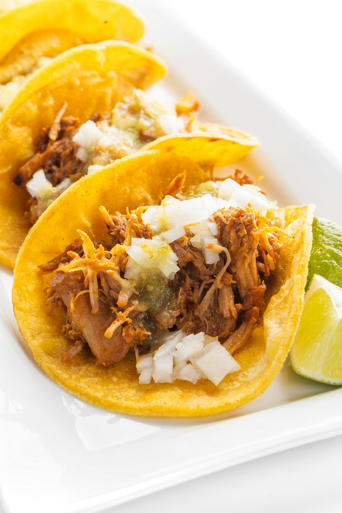 Three slow cooker tacos al pastor on a plate topped with diced onion and green salsa.