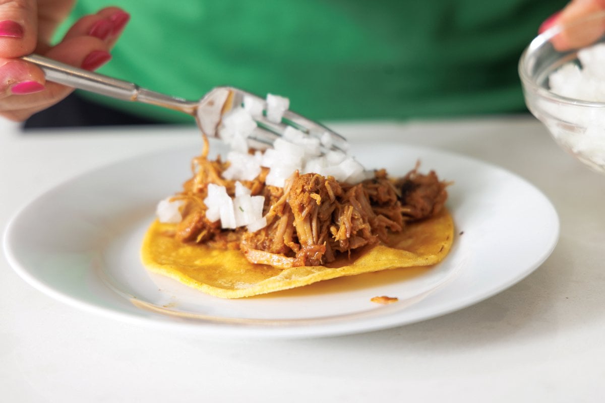 Assembling al pastor taco on corn tortilla.