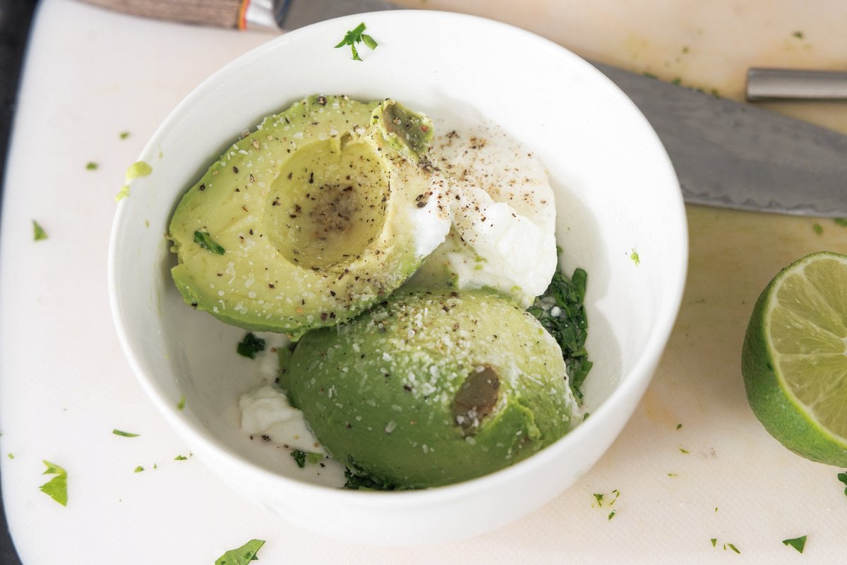 Halved avocado with plain yogurt and seasoning in a bowl.