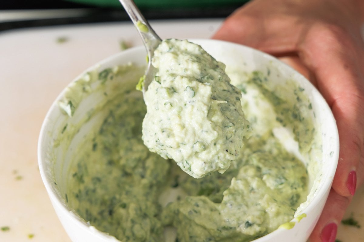 Fresh made avocado crema stirred in a white bowl with a spoon.