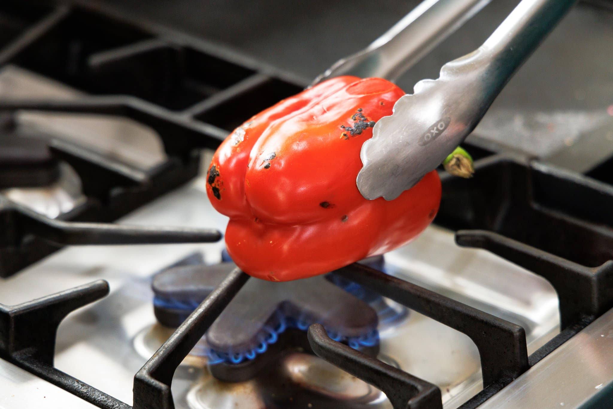 Using metal tongs to roast red bell pepper over an open flame.