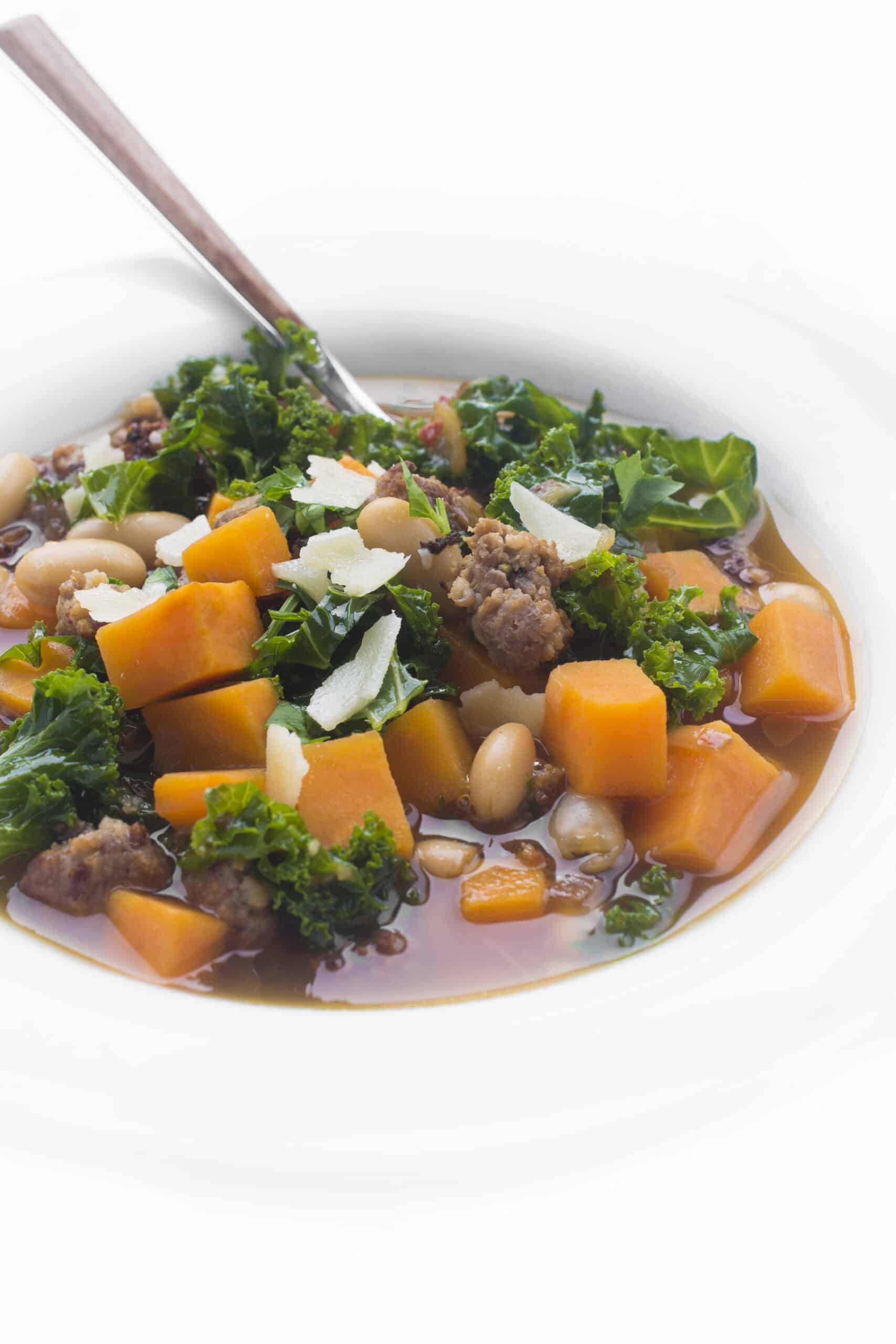 Bowl full of sausage, bean, and sweet potato soup with a spoon sitting on the edge.